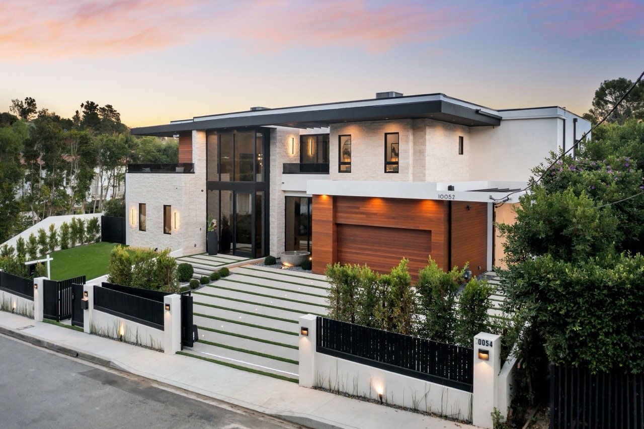 Modern luxury house exterior at sunset with green lawn and driveway in a suburban neighborhood.